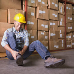 Worker with sprained ankle on floor in warehouse Male worker sitting with sprained ankle on the floor in warehouse